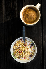Rustic Breakfast with muesli and cup of coffee on old dark woode