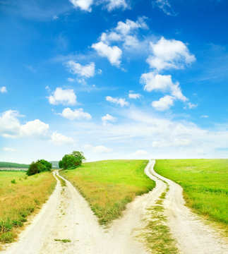 Fork in the road. A country road splits in two, making a decision that requires a fork in the road. Conceptual image. Blue summer sky with white clouds on it.