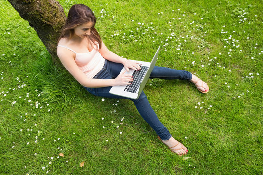 Beautiful Brunette Woman Leaning Against A Tree Using Her Notebo