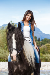 Obraz premium Young girl sitting on horse while crossing river in a mountainou