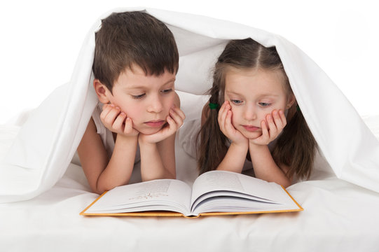 childs read a book in bed under the blanket
