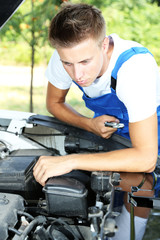 Fototapeta na wymiar Young auto mechanic repairing car engine outdoors