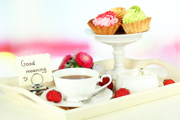 Cup of tea with cakes on wooden tray on table in room