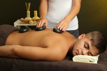 Fototapeta na wymiar Young man having stone massage in spa salon