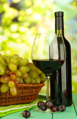Fototapeta na wymiar Ripe grapes in wicker basket, bottle and glass of wine,