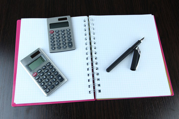 Notebook with pen and calculators on wooden background