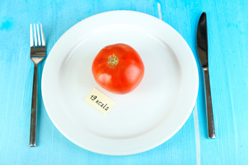 Calorie content of tomato on plate on wooden table close-up