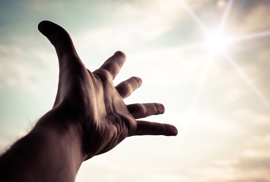 Hand of a man reaching to towards sky. Color toned image.