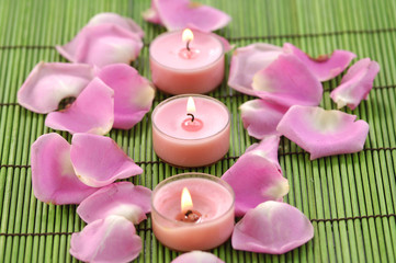 Spa composition of rose petals and row candle on green mat