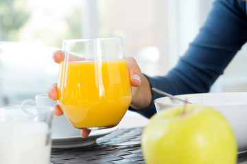woman's hand grabbing a glass of orange juice at breakfast