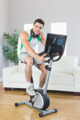 Fototapeta premium Smiling handsome man training on exercise bike using laptop