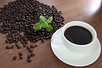 Coffee beans and green peppermint near a white coffee cup.