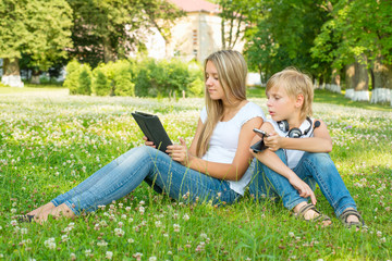 Naklejka na ściany i meble Boy and girl sitting in the park and enjoy the tablet
