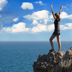 Obraz premium Happy woman with arms raised against blue sky with clouds