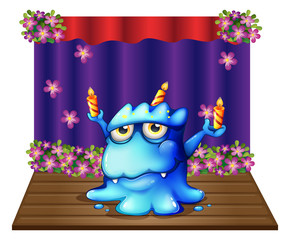 A stage with a blue monster balancing the three lighted candles