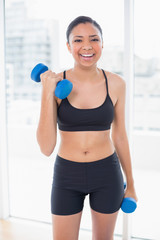 Laughing dark haired model in sportswear exercising with dumbbel