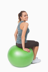 Fototapeta na wymiar Young woman sitting on fitness ball looking over shoulder at cam