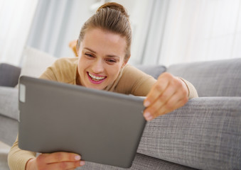 Smiling young woman using tablet pc while laying on sofa