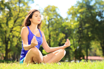 Naklejka na ściany i meble Young female athlete in sportswear meditating in a park