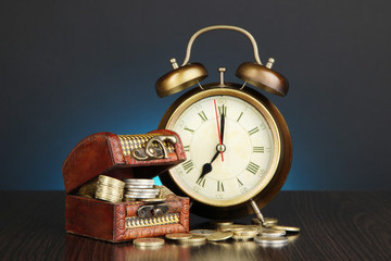 Antique clock and coins on wooden table on dark color