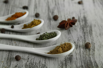 Assortment of spices in  white spoons, on wooden background