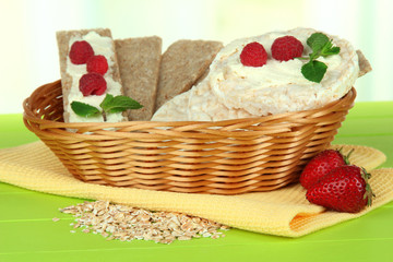 Tasty crispbread with berries in wicker basket, on green table