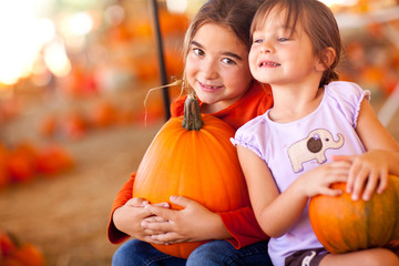 Fototapeta premium Adorable Little Girls Holding Pumpkins At A Pumpkin Patch