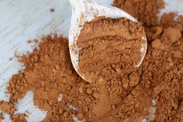 Cocoa powder in spoon on wooden background