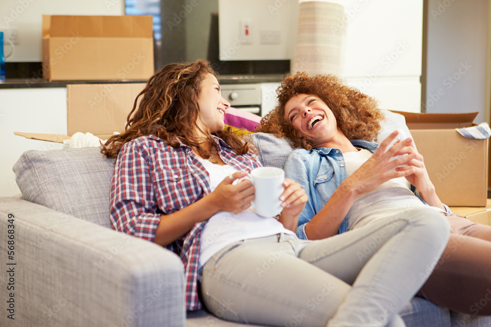 Wall mural Two Women Relaxing On Sofa With Hot Drink In New Home