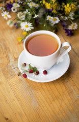 cup of aromatic tea, some berries of wild strawberry, bouquet of