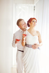 Naklejka premium bride and groom drinking wine at home in light interior (soft fo