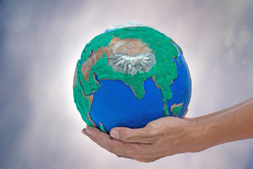 man his hands holding globe made from clay on gray lurid sky