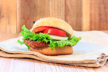 fish burger sandwich with lettuce and tomato on wood background