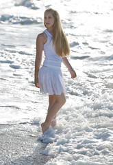 Young woman in white dress walking on the beach.