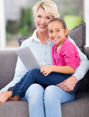 Obraz premium little girl sitting on grandmother's lap with notebook computer
