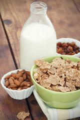 A bowl of cereal with almonds, milk and dried grapes