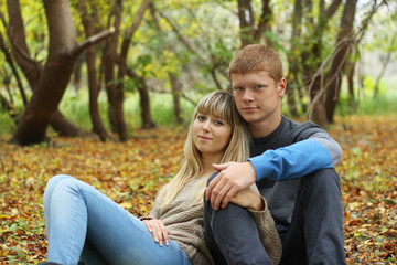 Young couple sitting on the foliage in autumn park