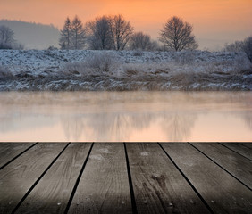 Fototapeta na wymiar Winter sunrise over the river and empty wooden deck table.