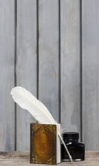 Ancient writer's desk - book, feather, ink on wooden rough surfa