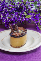 Cappuccino cake on white plate. Purple flowers in the background