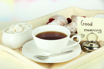 Cup of tea with cakes on wooden tray on table in room