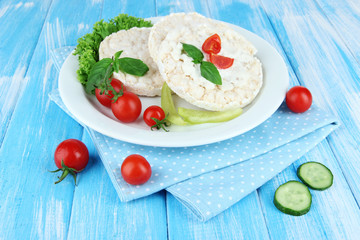 Tasty crispbreads with vegetables on blue wooden background
