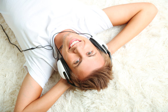 Young Man Relaxing On Carpet And Listening To Music