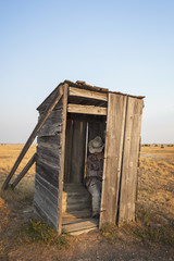 Mannequin sitting in old wooden outhouse