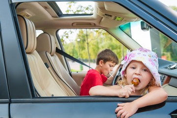 Two kids is going by car without parents. Girl eats candy, boy d