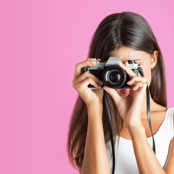 Woman with camera close up against pink background.