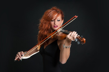Young woman playing violin against black background.