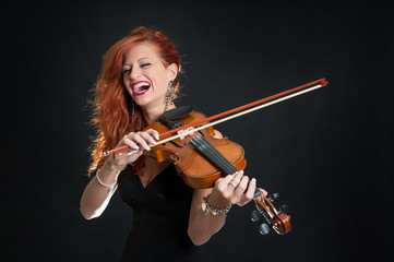 Young woman playing violin against black background.
