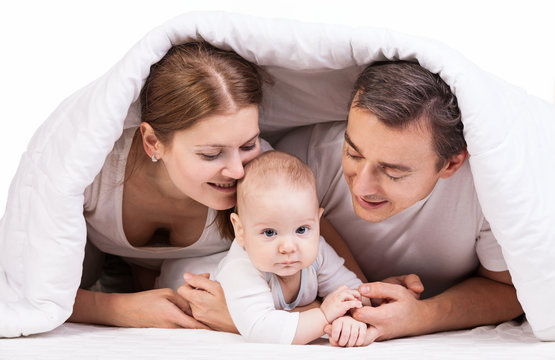 Young Family With Baby Boy Under Blanket On Bed