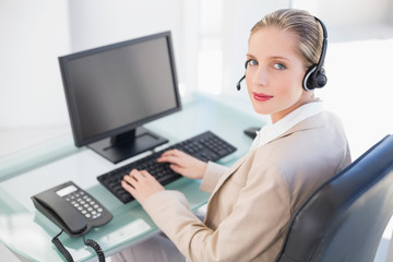 Blonde call centre agent typing looking at camera